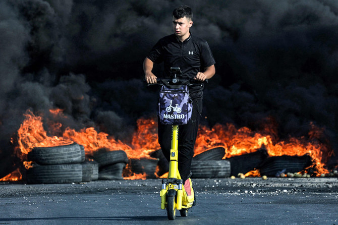 2023年10月8日、ヨルダン川西岸地区のラマッラーで、イスラエル軍との衝突で火が付いたタイヤの中を、スクーターで通り過ぎるパレスチナ人デモ参加者。（AFP）