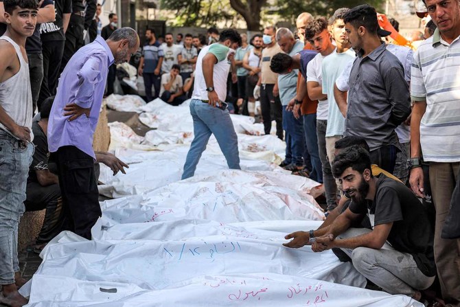 イスラエルの空爆による犠牲者の遺体の傍に立つ人々。2023年10月12日、ガザのアル・シファ病院の遺体安置所の外。（AFP）