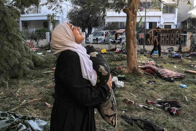  2023年10月18日、ガザ中心部のアフリ・アラブ病院跡地の外で、瓦礫の中にたたずみ、枕を抱えて涙を流す女性。(AFP＝時事）