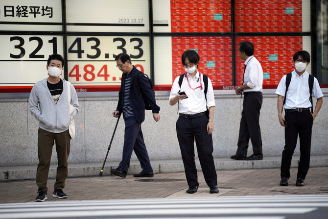 東京の証券会社の日経平均株価を表示する電子株価ボードの前に佇む人々。2023年10月17日。（AP通信）