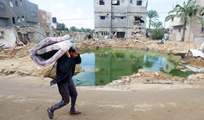 パレスチナ人が、ガザ地区中央部のヌセイラット難民キャンプで、イスラエルの爆撃により破壊された建物の前を歩いていく。 (AP)