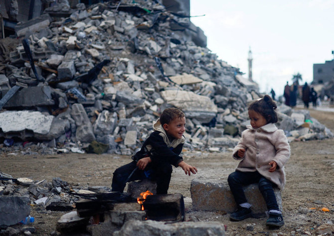 2023年11月27日、ハマスとイスラエルが一時休戦する中、ガザ南部でイスラエル軍の空爆を受けた家屋の瓦礫の横で、火のそばに座るパレスチナの子供たち。(Reuters）