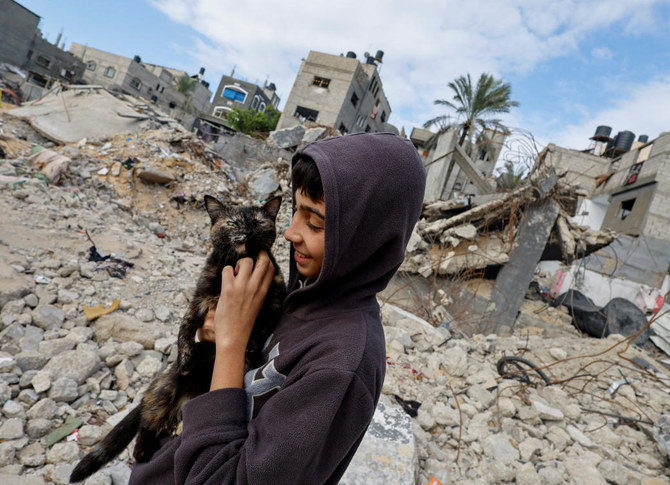 2023年11月27日、ハマスとイスラエルが一時休戦する中、ガザ南部でイスラエル軍の空爆を受けた家屋の瓦礫の横で、火のそばに座るパレスチナの子供たち。(Reuters）