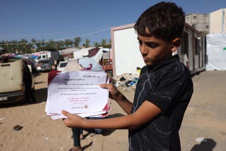 4日間の停戦が発効した2023年11月24日、数週間にわたる攻撃が続いたガザ地区南部のハーンユーニスで、ガザ地区北部には戻らないよう市民に警告するイスラエルのチラシを持つパレスチナ人の少年。（AFP）