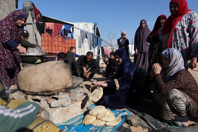 イスラエルの攻撃のため自宅から逃げたパレスチナ人避難民たちがラファのキャンプに避難する中、女性が食べ物を準備するのを待つ人々。（ロイター）