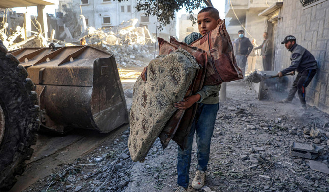 イスラエルとハマスの戦闘が続く中、15日、ガザ地区南部で破壊された建物の瓦礫をトラクターで片付けながら、枕を運ぶパレスチナの少年。(AFP)