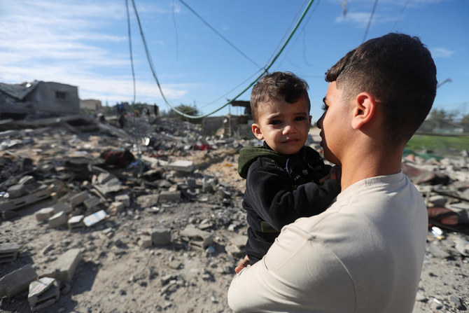 イスラエルとパレスチナのイスラム主義組織ハマスとの間で紛争が続く中、ガザ地区南部のラファで、イスラエルによる民家への空爆現場を子供を抱いて見つめるパレスチナ人。（Reuters）