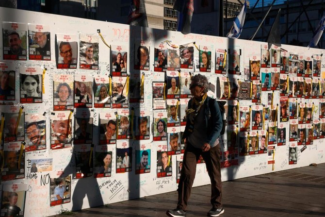 イスラエルとパレスチナの過激派組織ハマスとの戦いが続く中、テルアビブの壁に貼られた肖像画の前を通り過ぎる人々。そこには、パレスチナのハマス戦闘員による10月7日の攻撃以来ガザで拘束されている、イスラエルの人質が描かれている。(AFP)