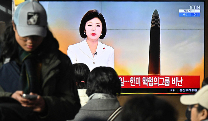 2023年12月18日、ソウルの鉄道駅で、北朝鮮のミサイル発射実験に関するニュース映像を映し出すテレビ画面の近くに座る人々。(AFP＝時事）