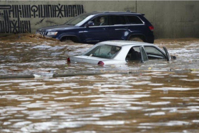 2023年12月23日、ベイルート内で、雨で冠水した高速道路で、冠水した車の前で自分の車を運転する男性が背景に写る。(AP)