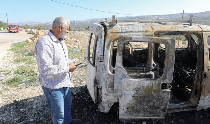 ヨルダン川西岸地区で、入植者の襲撃によって燃やされた車両を確認するパレスチナ人。（ロイター）