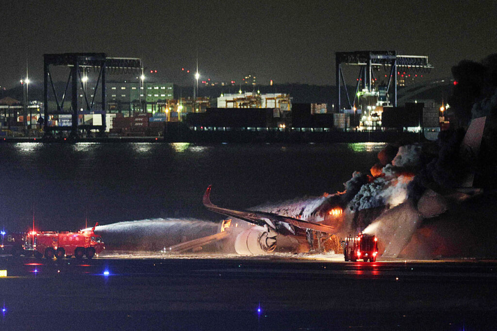 時事通信提供の写真は、羽田空港の滑走路で日航機の火災を消火しようとする消防隊員（2024年1月2日撮影）。- 1月2日、東京・羽田空港の滑走路で、海上保安庁の航空機と衝突したとみられる日航機が炎上しているとテレビが報じた。(時事通信／AFP＝時事） 