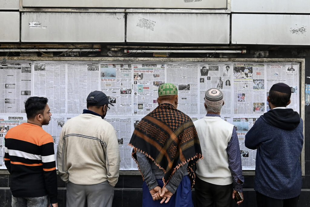 2024年1月7日に予定されているバングラデシュ総選挙を前に、4日、ダッカの通り沿いでボードに掲げられた新聞を読む男性たち。(AFP＝時事）