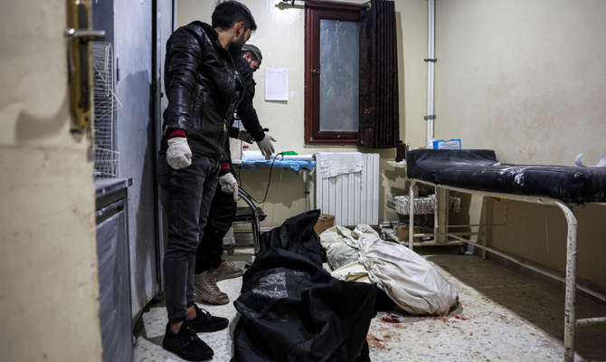反体制派の支配する町の病院で、シリア政府軍によるとされる爆撃の余波で死亡した2人の犠牲者の遺体の前で立ち尽くす人々。シリア北西部イドリブ県、2023年12月30日。（AFP）