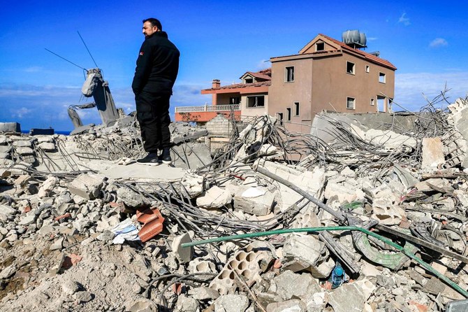 2024年1月4日、イスラエル北部との国境に近いレバノン南部の町ナクラへの砲撃後、破壊された建物のがれきの中に立つ男性。（AFP）