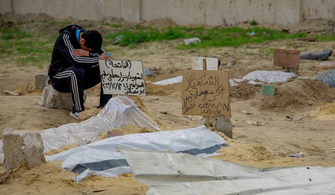 2024年1月9日、ガザ市アルシャビヤ地区近くの住宅街にある仮設墓地に遺体が並ぶなか、イスラエルの爆撃で亡くなった人の浅い墓のそばに座る若者。（AFP）