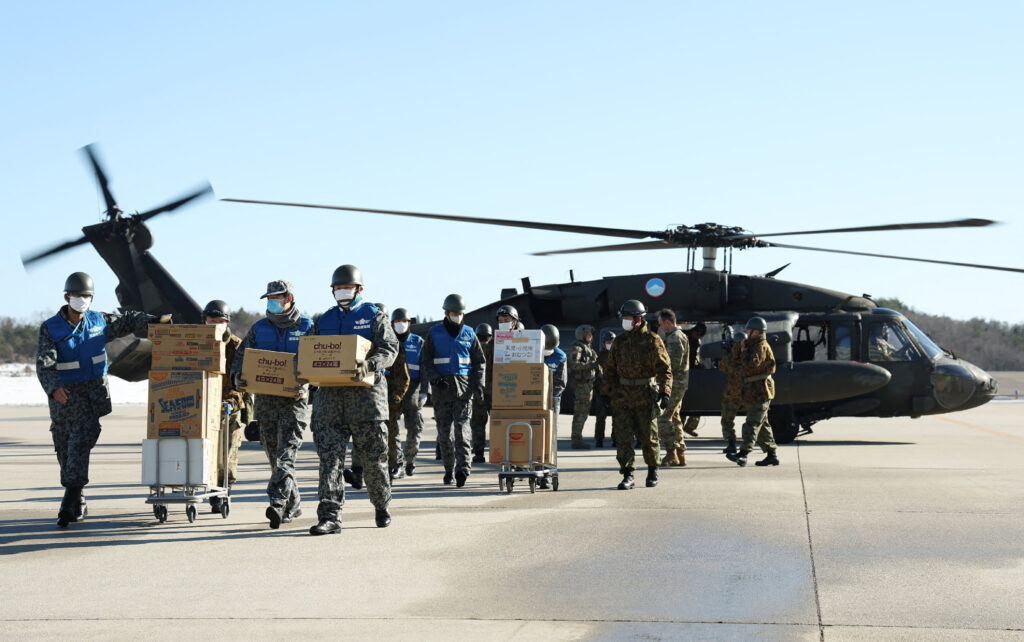 石川県輪島市の能登空港で、米軍ヘリから被災者への救援物資を運ぶ自衛隊員（2024年1月17日撮影）。 (AFP＝時事）