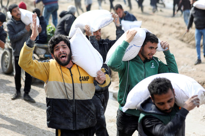 ガザ住民が危機的レベルの飢餓に直面する中、イスラエルの検問所付近で支援トラックから受け取った小麦粉の袋を運ぶパレスチナ人（2024年2月19日、ガザ市）。(ロイター）