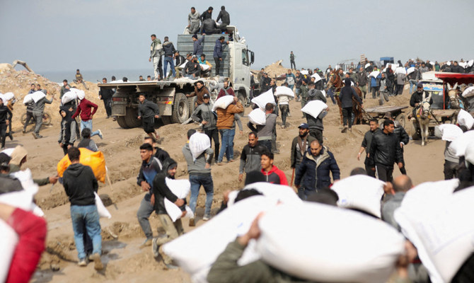 イスラエルの検問所近くで援助トラックから奪った小麦粉の袋を運ぶパレスチナ人。ガザ市でイスラエルとハマスの紛争が続く中、ガザ住民の飢餓状態は危機的レベルに達している。2024年2月19日撮影。（ロイター）