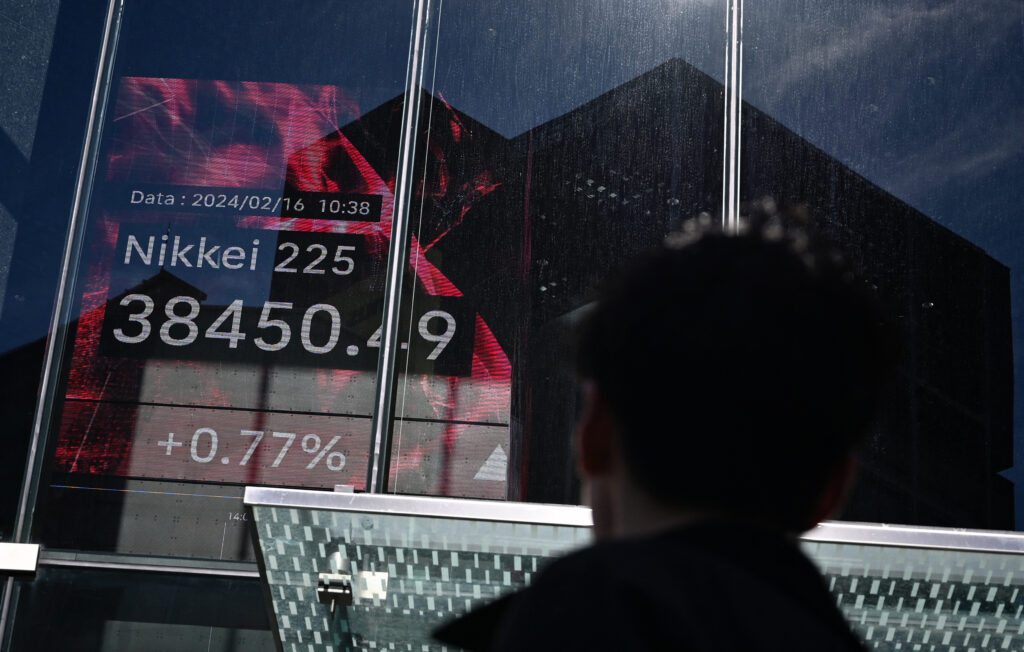 2024年2月16日、東京で、東京証券取引所の株価を示すモニターの前を歩く男性（撮影：Kazuhiro NOGI / AFP）
