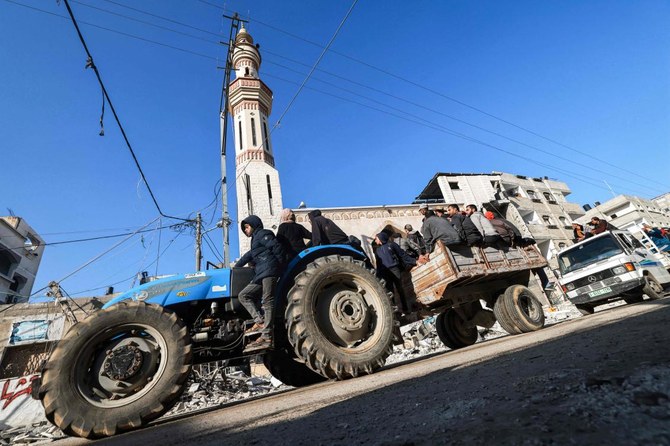 イスラエルとパレスチナの武装組織ハマスの間で紛争が継続する最中、ガザ地区南部のラファで破壊された建造物の瓦礫とモスクのミナレットの前を通過するトラクターが牽引する荷車に乗っている人々。(AFP)