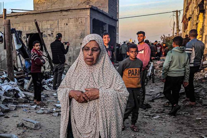 2024年2月11日、イスラエルとパレスチナの武装組織ハマスの対立が続く中、ガザ地区南部のラファで、イスラエル軍の砲撃により大きな被害を受けた建物の近くにいる若者たちを通り過ぎる高齢の女性。（AFP）