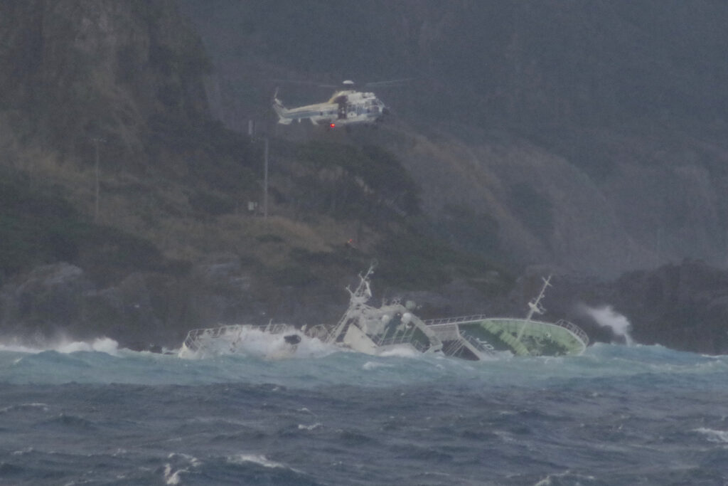 海上保安庁提供の写真で、東京の南西に位置する神津島沖で、ほぼ横に傾いた漁船を救助するため、海上保安庁のヘリコプターがホバリングしている（2024年3月4日月曜日）。東京の南西に位置する伊豆諸島付近で、エンジントラブルのため座礁したマグロ漁船。( Japan Coast Guard via AP)
