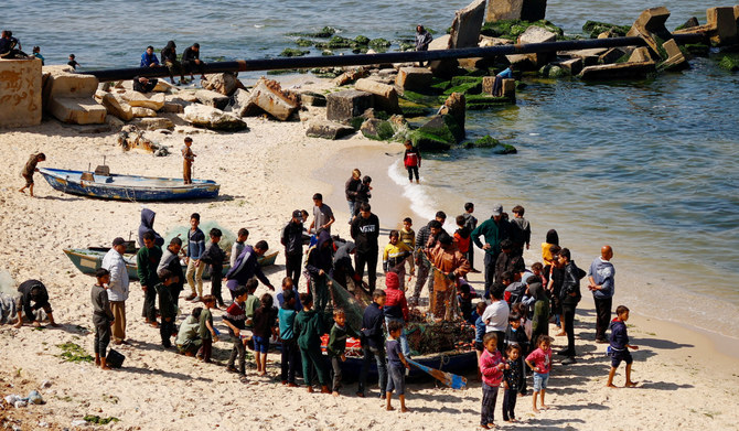 2024年2月26日、ガザ地区南部のラファで、イスラエルとハマスの対立が続く中、漁師が浜辺で網から魚を取り出す際に集まるパレスチナ人。(REUTERS)