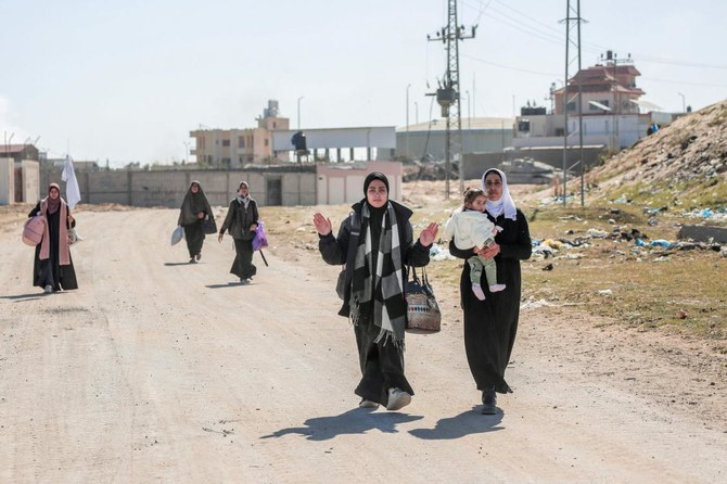 2024年3月5日、ガザ地区南部ハーン・ユーニスのハマド・シティ地区を脱出する際、イスラエル軍の横を通り過ぎる際、荷物を持った避難民のパレスチナ人女性たちがその場しのぎの白旗を掲げる。(AFP＝時事）