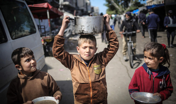 木曜日、ガザ地区南部のハーン・ユーニスで、食料配給所に向かって歩きながら台所用品を運ぶ若者たち。(AFP＝時事）