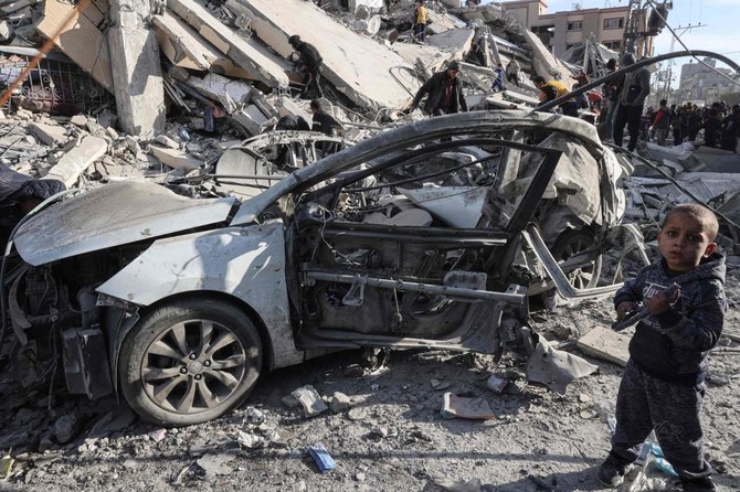 2023年3月9日、ガザ地区南部のラファで、イスラエル軍の空爆で破壊された住宅のがれきの中で、壊れた車の横に立つパレスチナ人の少年。(AFP＝時事）