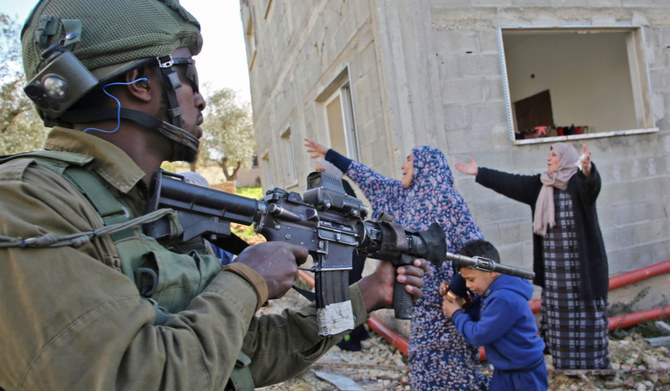 ヨルダン川西岸地区ナブルス近郊のクファル・カドゥム村で、イスラエルによるパレスチナ人土地の収用に反対するデモの後、イスラエル軍に拘束された青年に別れを告げ、抗議するパレスチナ人女性たちに対し、アサルトライフルを構えるイスラエル軍兵士。(AFP＝時事）