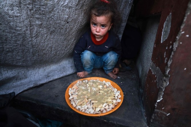 ガザ地区南部のラファで、皿の横に座るパレスチナ人の子ども。(AFP）