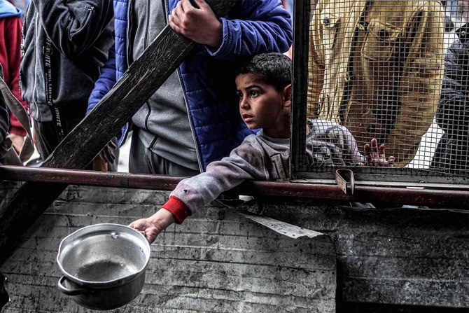 2024年3月16日、ガザ地区南部のラファで、イフタールを前に空の鍋を差し出す少年。(AFP）