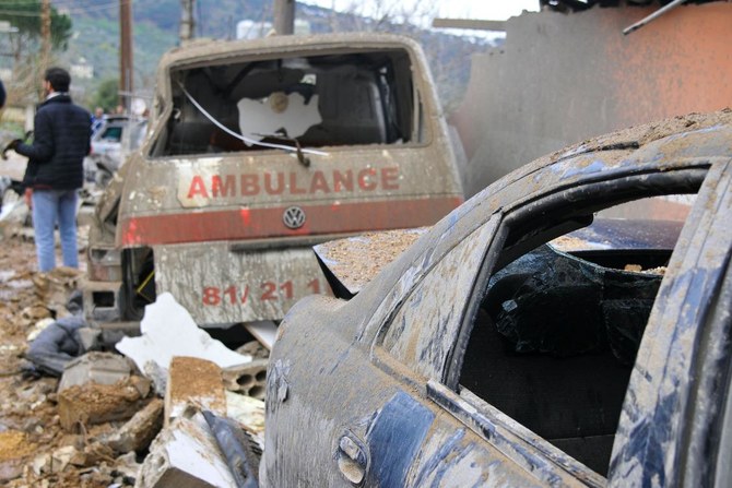 イスラエル国境近くのヘッバリエで一晩中行われたイスラエル軍の空爆で、損壊した救急車と車の横に立つ男性（2024年3月27日撮影）。(AFP＝時事）