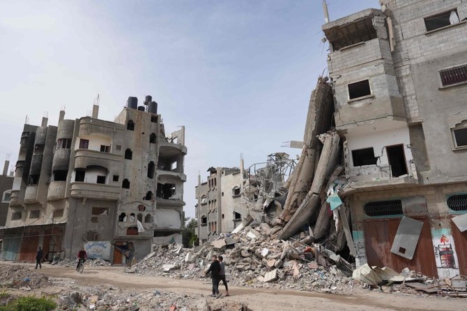 2024年3月29日、ガザ地区中央部にあるパレスチナ難民のためのマガジキャンプで、損壊し破壊された建物を通り過ぎるパレスチナ人。(AFP＝時事）