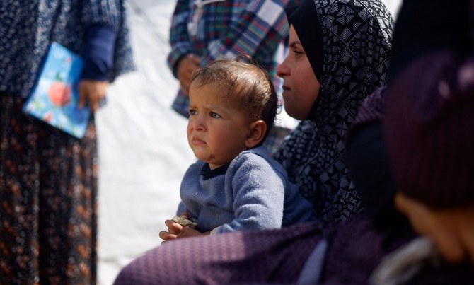 2024年3月6日、ガザ地区南部ラファのパレスチナ人避難民キャンプで、子供と座る女性。(ロイター）
