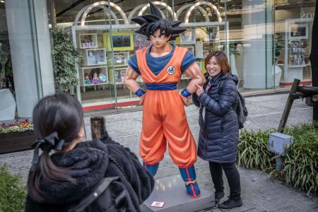 ドラゴンボールのキャラクター「孫悟空」の像と写真を撮る女性（2024年3月8日、東京都内で）。(AFP＝時事）