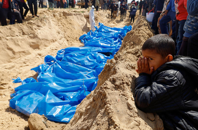 イスラエルとパレスチナのイスラム主義組織ハマスの対立が続く中、イスラエルによる空爆や銃撃で死亡したパレスチナ人の遺体がイスラエルによって解放された後、ラファの集団墓地に埋葬されるのを見守る子ども（REUTERS）。