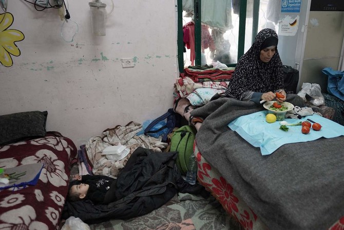 2024年4月3日、ガザ地区中部のデイル・アル・バラにあるシュハダ・アル・アクサ病院で、寝ている少年のそばで野菜を切るパレスチナ人女性。(AFP＝時事通信）