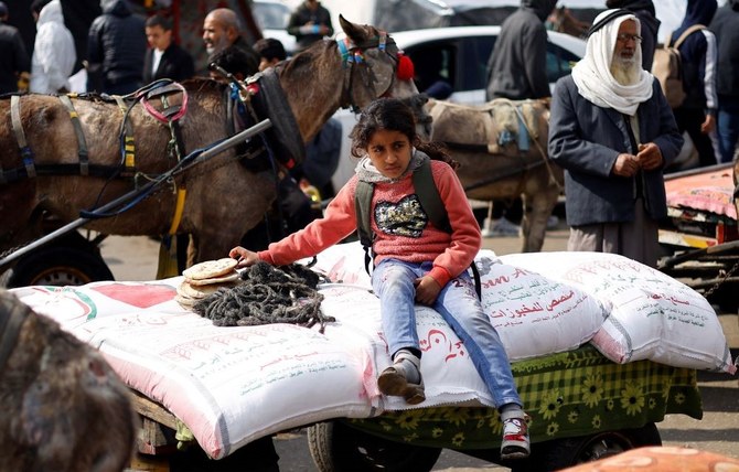 イスラエルとハマスの紛争が続く中、国連パレスチナ難民救済事業機関（UNRWA）が配布した小麦粉の袋の上に座るパレスチナ人の少女（ガザ地区南部ラファ、2024年1月29日）。(ロイター）