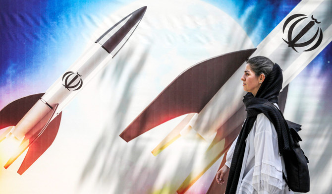 2024年4月15日、テヘラン中心部で、イラン・イスラム共和国の国章をあしらったミサイル発射の横断幕の前を歩く女性。(AFP＝時事）