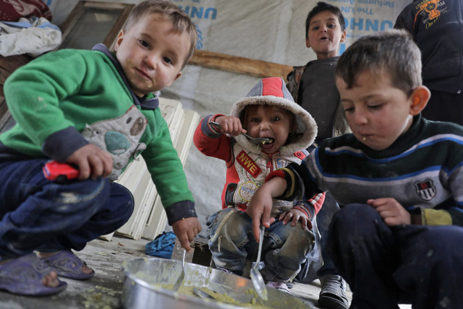 2018年1月26日、レバノンのベカー渓谷にある町ザーレ郊外の難民キャンプで、テントの床に置かれた鍋で一緒に食事をするシリアの子どもたち。(AFP＝時事）