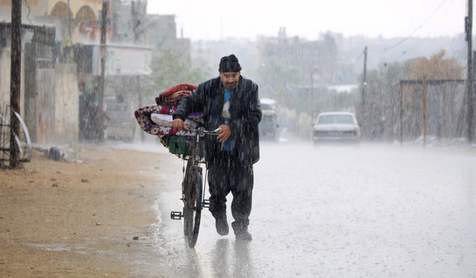 2024年5月6日、イスラエルとパレスチナ・ハマスの対立が続く中、イスラエル軍による避難命令が出されたガザ地区南部のラファで、雨の中、荷物を載せた自転車を押す避難民のパレスチナ人男性。(AFP＝時事）