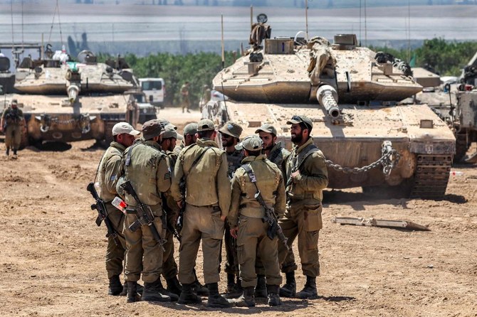 2024年5月9日、イスラエルとハマスの紛争が続く中、イスラエル南部のガザ地区との国境近くに配置された主力戦車の前に身を寄せるイスラエル軍の兵士たち。(AFP＝時事）