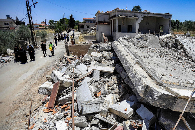 2024年6月21日、イスラエルとの国境に近いレバノン南部のヤルーン村で、イスラエル軍の砲撃により破壊された建物の瓦礫の前を歩く人々。(AFP＝時事）