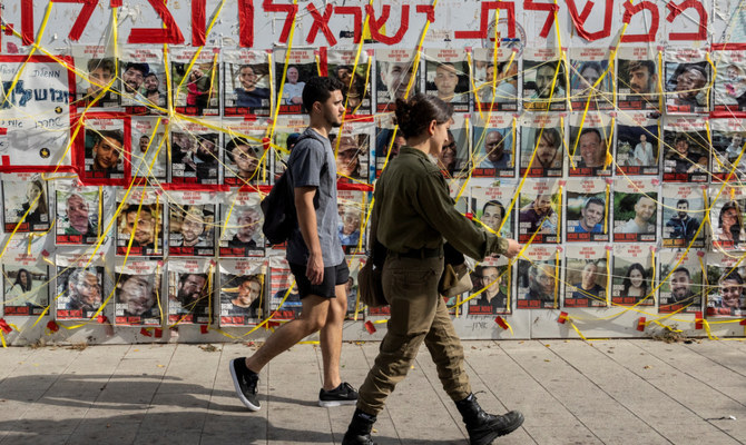 2024年6月24日、イスラエルのテルアビブで、ハマスによる10月7日のイスラエル攻撃で誘拐された人質のポスターの横を歩く人々。(ロイター）