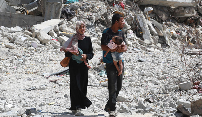 2024年7月4日、イスラエルとパレスチナ過激派組織ハマスの対立が続く中、ガザ地区南部のハーン・ユーニスで、がれきの中を歩くパレスチナ人夫婦が子どもを抱いている。(AFP=時事)
