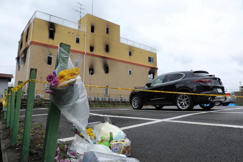 2019年7月19日、京都で前日に火災が発生し、少なくとも33人が死亡した京都アニメーション社のスタジオ(奥)付近で、花や供え物が写真に収まる。(AFP=時事)