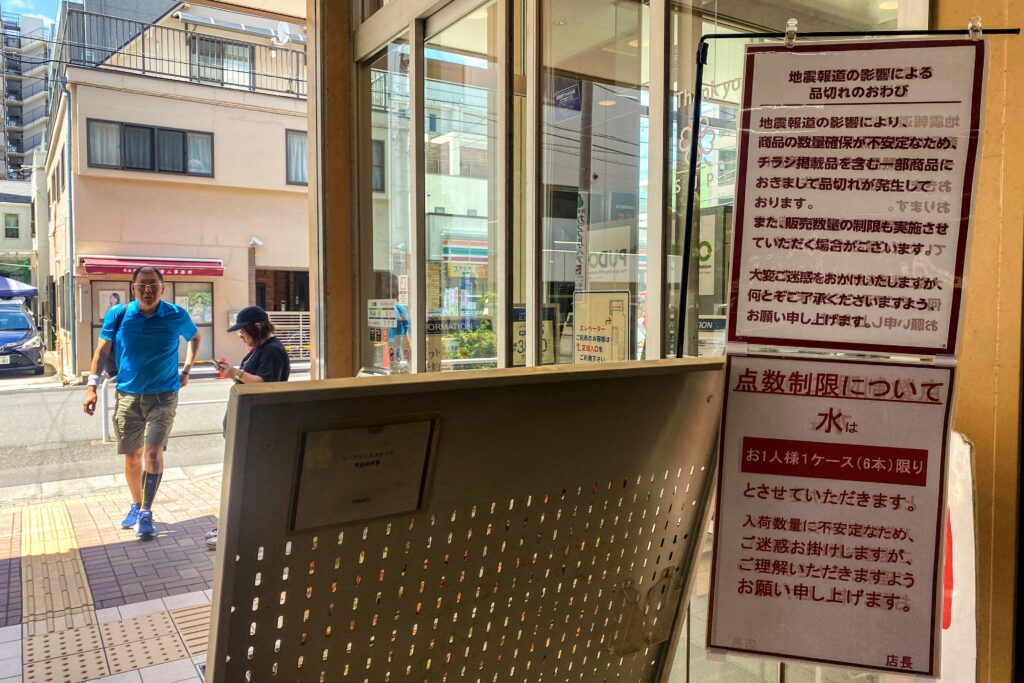 東京・墨田区で2024年8月10日、「地震関連の報道により、品切れの商品もあり、販売制限がかかる可能性がある」(上)、「ペットボトルの水は配給制で、1人1ケース(6本)まで」と書かれた看板が立ち並ぶスーパーの入り口を通る客。(写真:Philip FONG / AFP)